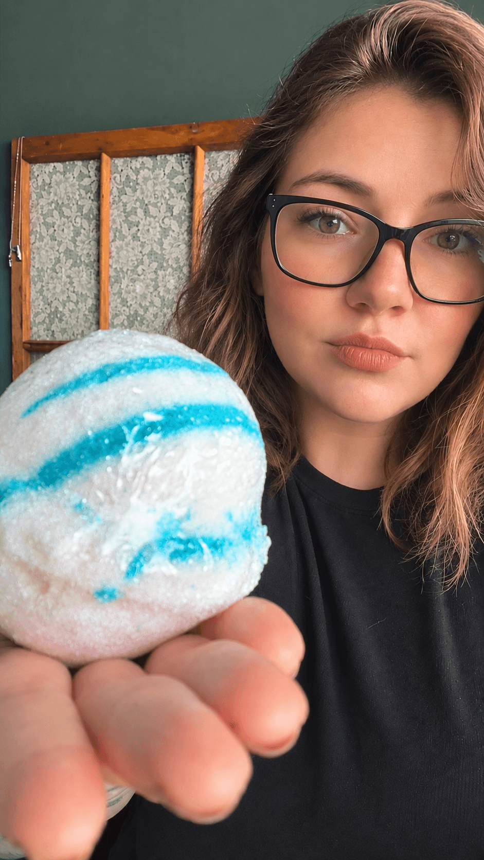 The maker of Verdant Vitals holding out a large white and turquoise swirled bath bomb